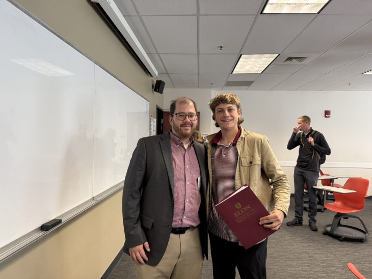 David Jiang stands with Elon alumnus Kerek Myers, who holds a Love School of Business folder.