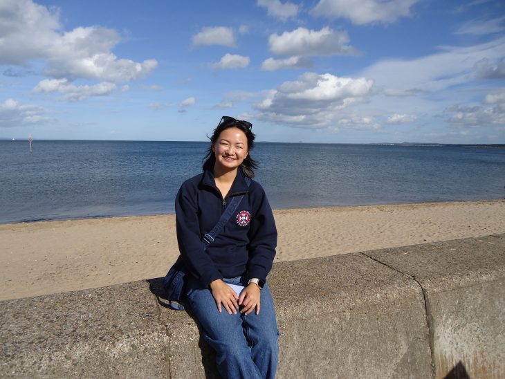 A woman sits on a wall in front of a beach