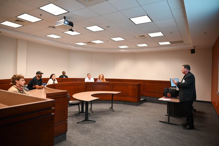 A speaker leads a small-group discussion with attendees seated around a classroom.