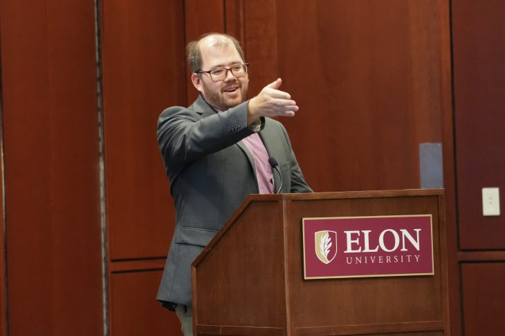 David Jiang speaks from a podium and gestures toward the audience.