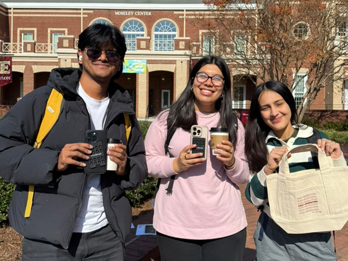 Three students pose while hold first-gen prizes in front of Moseley.