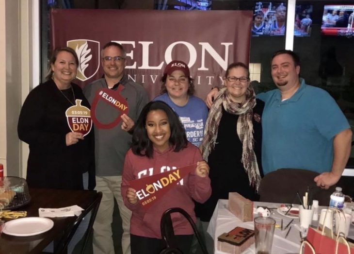 Kat Wallace, Crystal Moyer, Chris Wallace and other Elon alumni gather in front of an Elon University banner during an Elon Day event in Jacksonville.