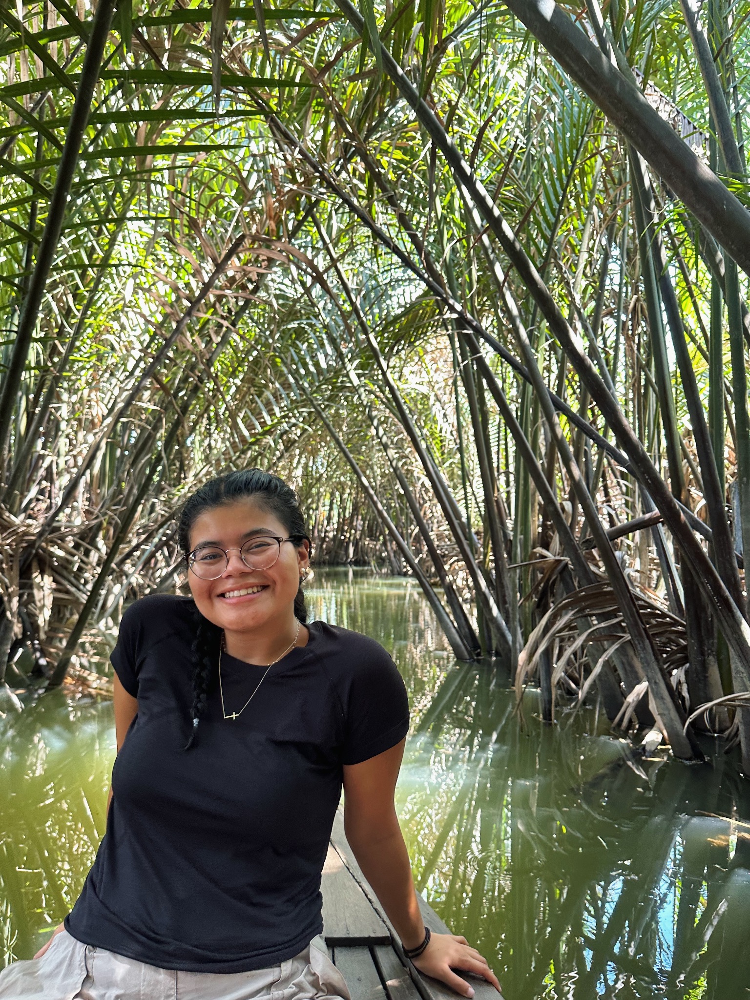 Jocelyn Gomez ’27 smiles from a wooden boat beneath arching palms over a narrow green waterway.