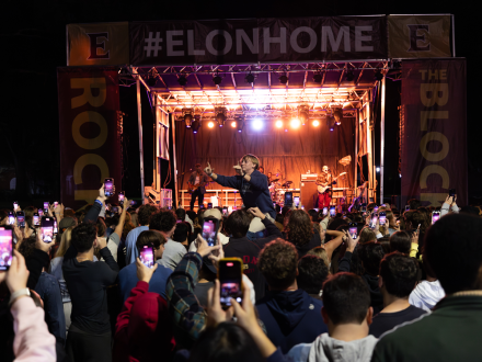 Crowd recording a band on phones at Elon's Homecoming concert, one person raised on shoulders above the crowd.