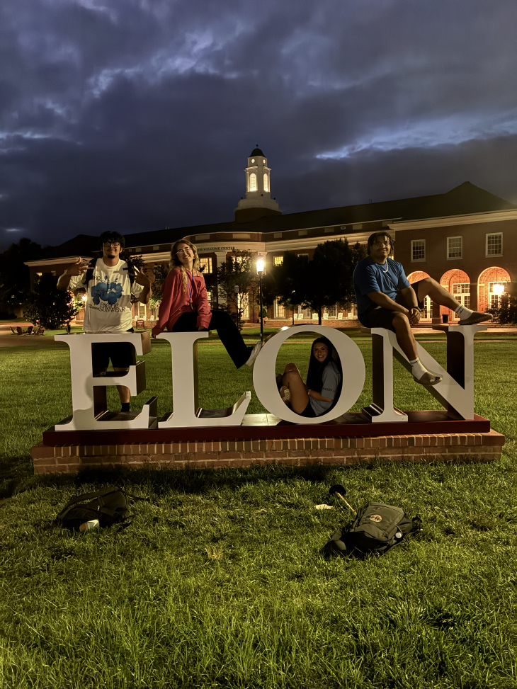 Josh Cox sits on the N while three fellow students pose around the ELON letters at night.