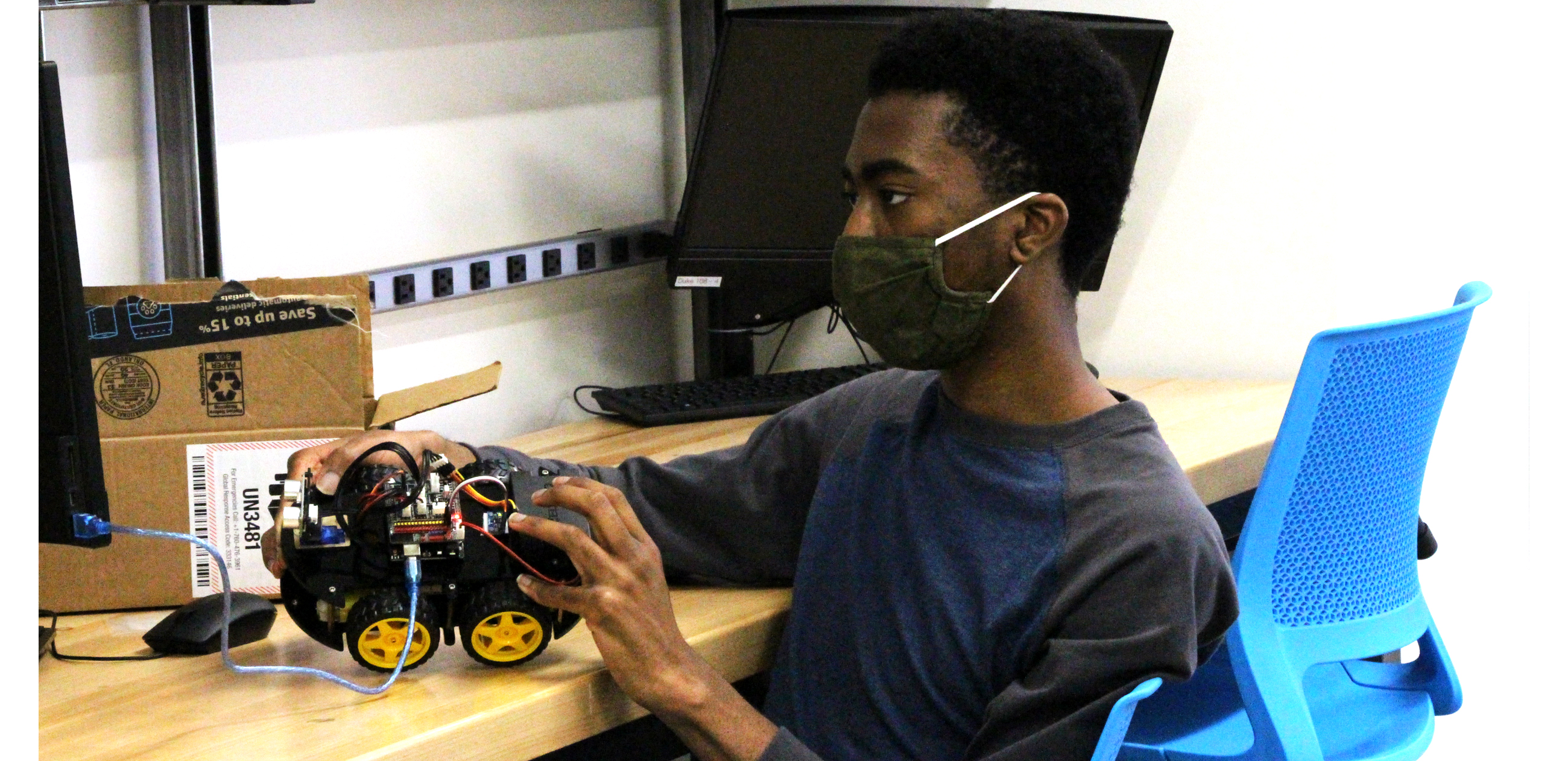 Black male student building a robotic vehicle in a robotics lab.