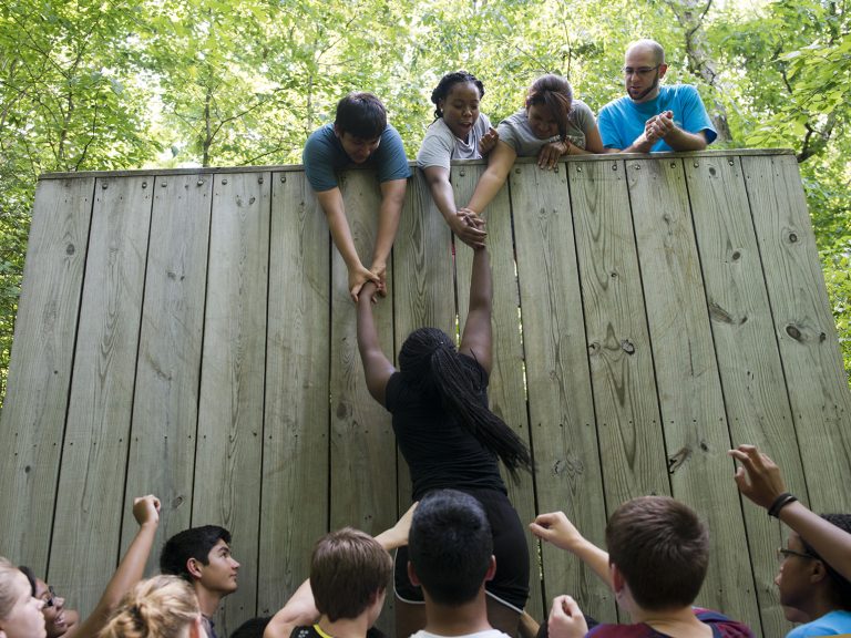 A group of students help a female student climb a wall