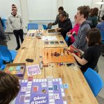 Group of students stand around table with their respective colorful custom made board games