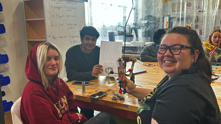 Three students holding up a character made from scrap materials
