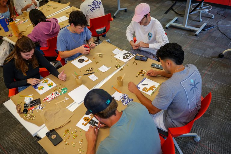 5 students around a table each working on their own mosaic