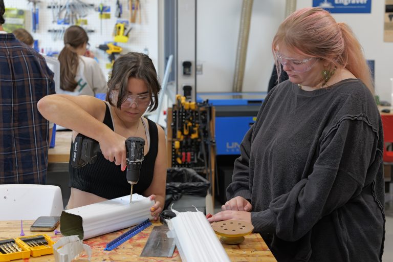 Student drilling hole inside device, made from aluminum rain gutters.