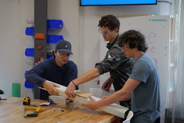 Three students putting rubber bands around their device.