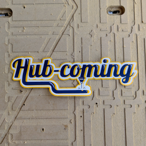 Hub-Coming! sticker on wooden background