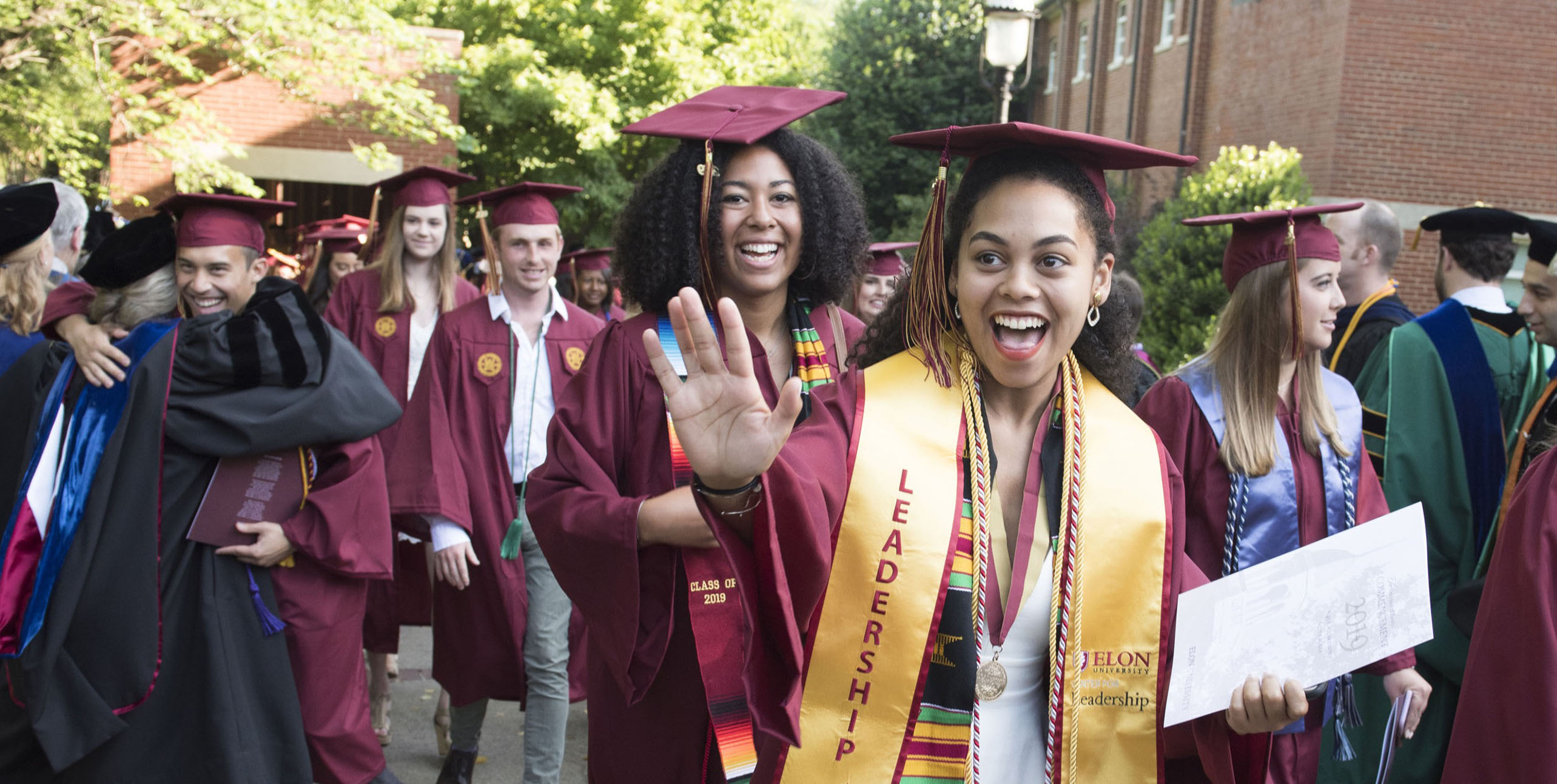 Graduates walk and wave during commencement at Elon