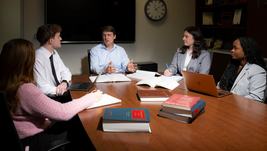 A professor meets with four students in a conference room. PreLaw Magazine names Elon Law is one of the best law schools in NC for practical training, women leadership and diverse students..