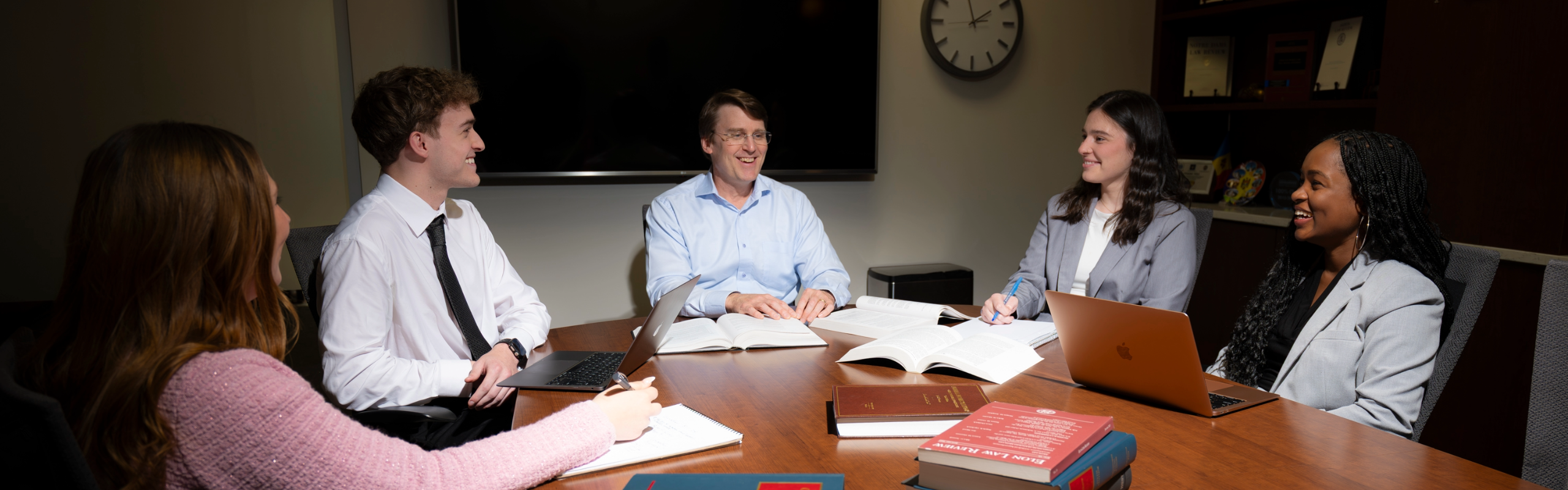 A professor meets in a conference room with a group of laughing, smiling students. PreLaw Magazine names Elon Law is one of the best law schools in NC for practical training.