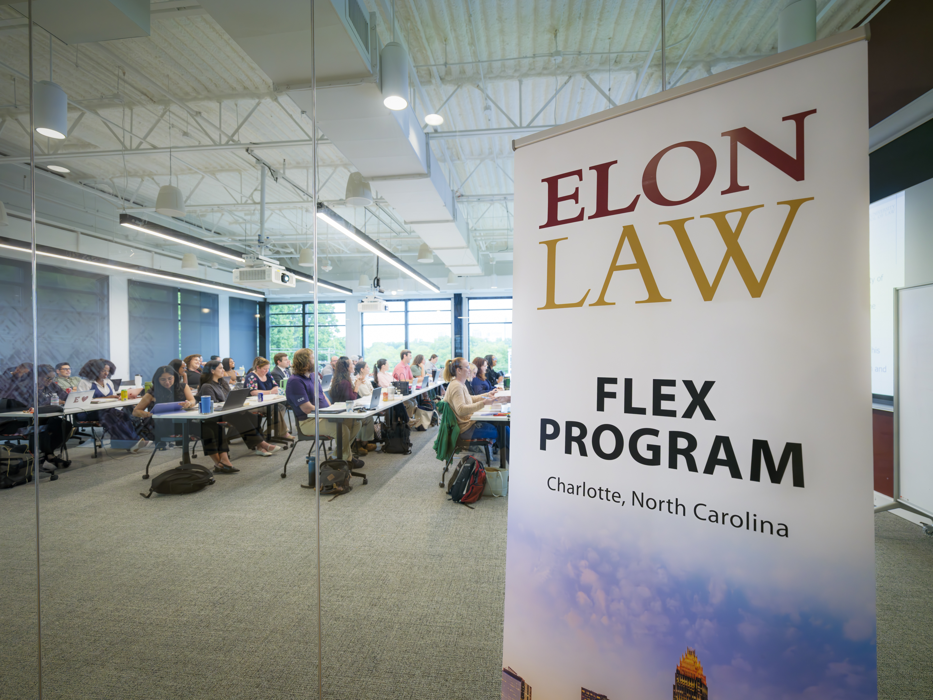 Students in a Charlotte classroom behind an Elon Law Flex Program banner. Elon Law offers law school in Charlotte and is one of the best law schools in nc for professional skills.
