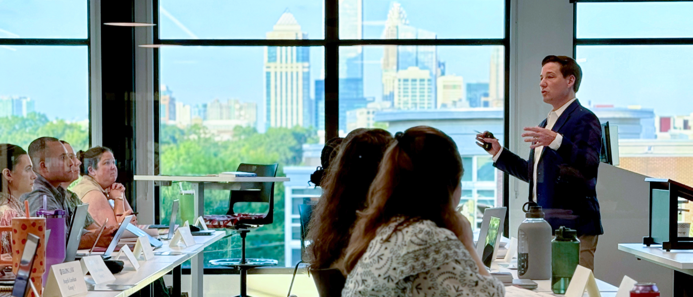 A law professor teaches in a large windowed classroom overlooking the Charlotte skyline. Elon Law operates a law school in Charlotte with full-time and part-time J.D. programs in one of the best law schools in NC for practical training.